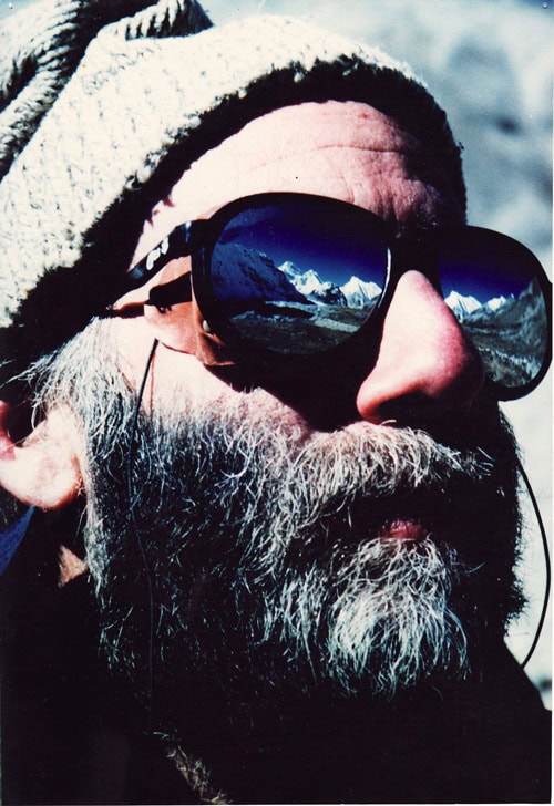 A man with a white beard and wearing dark sunglasses with a mountain reflection, donning a knit cap, appears to be in the snowy mountainous terrain of Nepal. The photograph seems evocative of family memories worthy of a photobook.
