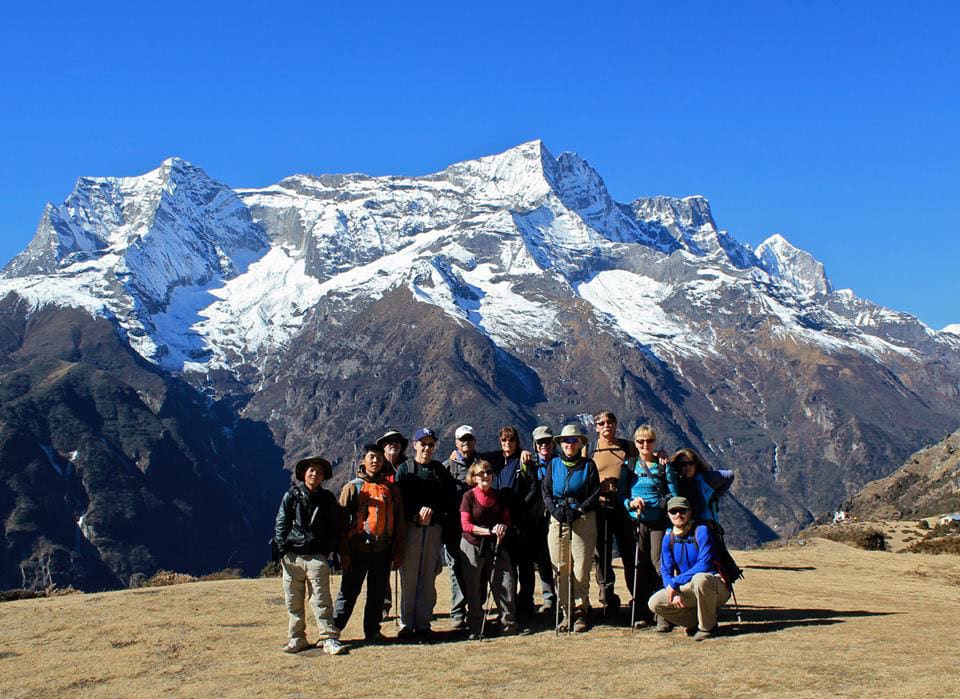 A family posing for a photo in front of a snow-covered mountain range in Nepal under a clear blue sky, perfect for the photobook.