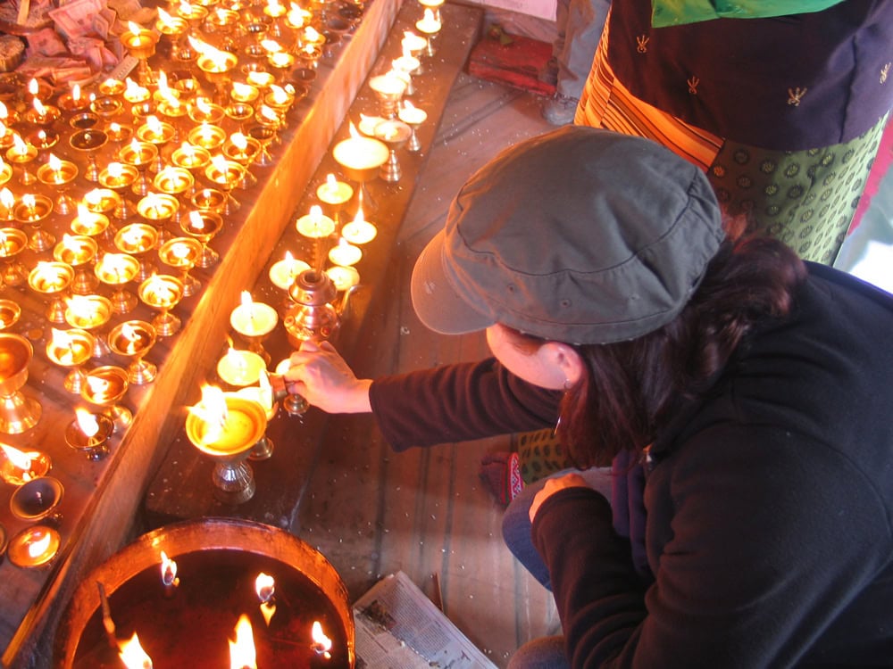 A person in a cap lights a candle from a row of burning candles in a dimly lit setting, akin to capturing a tranquil moment for a family photobook in Nepal.