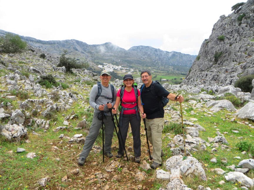 Three people with authentic hiking gear and trekking poles stand on a rocky trail in a mountainous landscape in Spain.