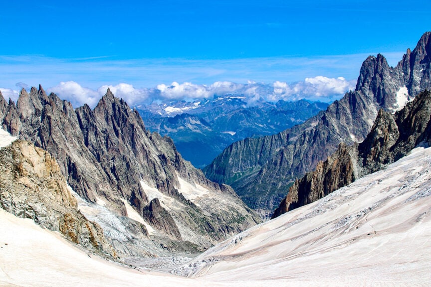 Rocky peaks and snow-covered slopes of a mountainous landscape with a clear blue sky capture the essence of the Tour du Mont Blanc, perfect for those seeking stunning trail photos.