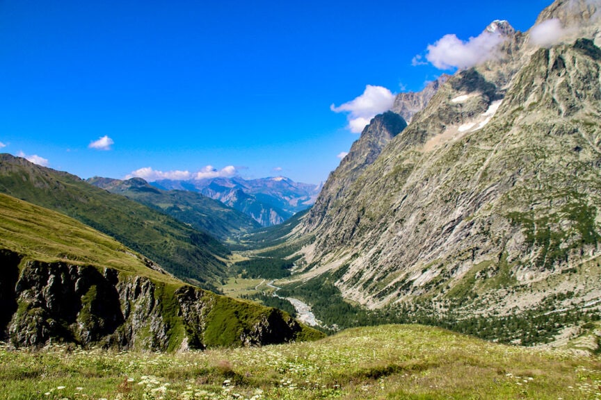 A mountain valley with a clear sky, rocky slopes, and grassy meadows. The scene shows a winding path through the valley surrounded by steep, rugged terrain, perfect for capturing trail photos on your Tour du Mont Blanc.