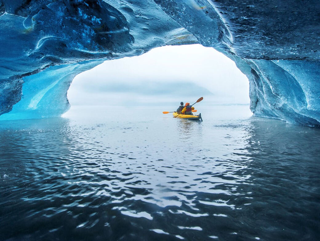 Two people in a yellow kayak paddle through an icy tunnel, emerging into a wide open body of water. This unforgettable experience highlights the awe-inspiring beauty of Alaska's Inside Passage and is a must for any travel enthusiast.