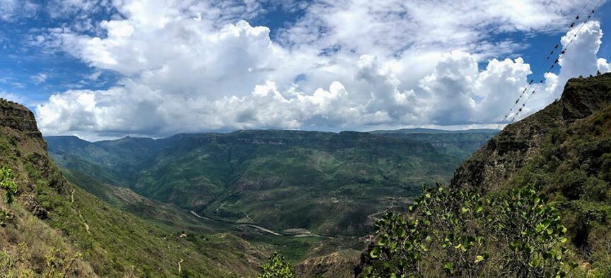 Panoramic view of a lush green valley in Colombia with mountains in the background under a partly cloudy sky. Sparse vegetation is visible in the foreground, promising amazing experiences for every visitor.