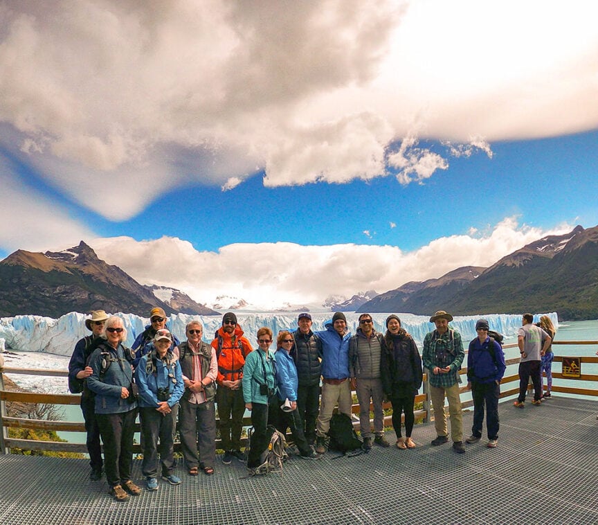 A group of people stands on a viewing platform with a glacier and mountains in the background under a partly cloudy sky, capturing the breathtaking beauty of Patagonia's national parks.