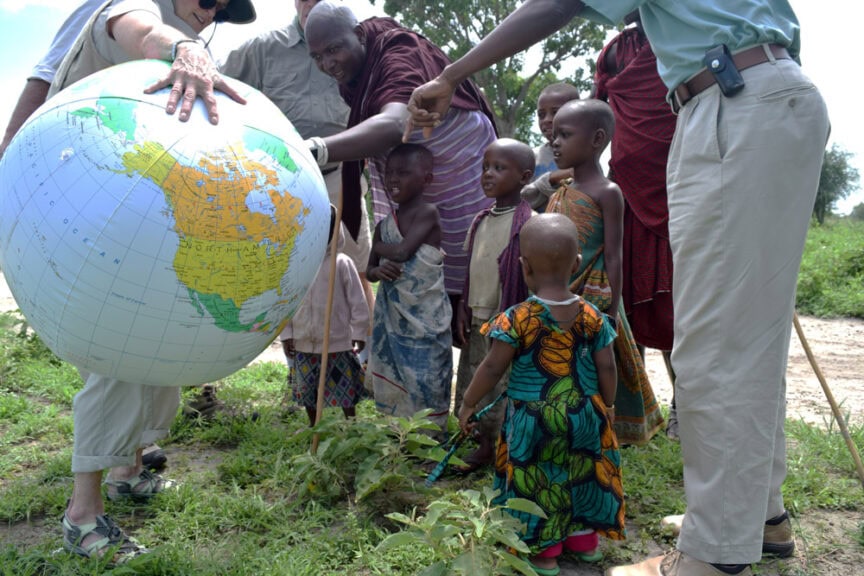 Several people, including children and adults, gather around and touch a large inflatable globe outdoors, exploring its surface with wonder.