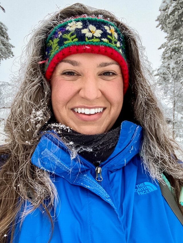 In Northern Finland, a person wearing a blue jacket and a colorful headband smiles brightly, ready for new adventures in the snowy landscape.