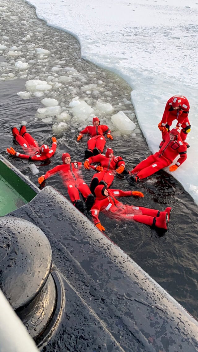 Six people in red immersion suits float on icy water near a ship's edge, surrounded by snow and ice in the heart of an adventure in Northern Finland.