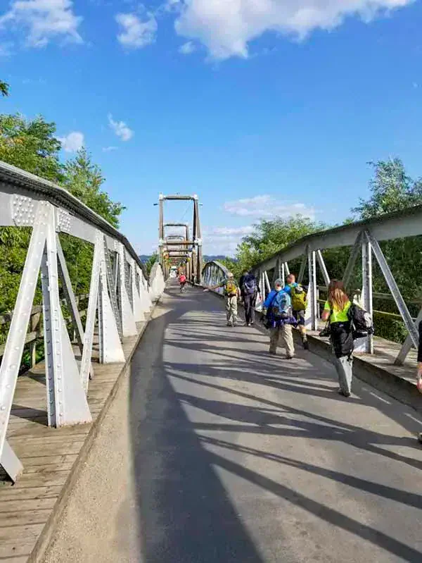 Under a blue sky with scattered clouds, people search for adventure as they walk across a steel truss bridge. It's a moment that echoes the spirit of the Carpathian Traverse, where roots of exploration and discovery run deep.