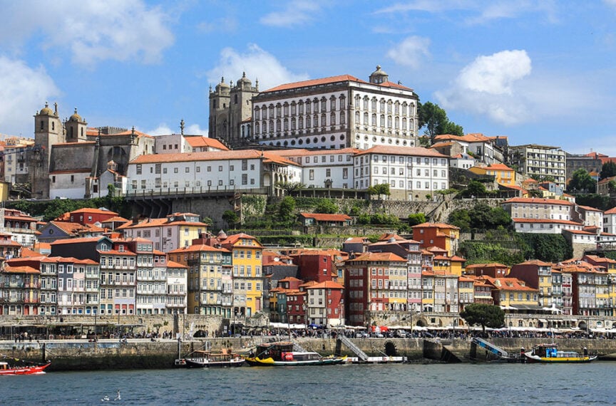 View of Porto, Portugal, showcasing colorful riverside buildings, historic architecture, and boats on the water beneath a blue sky, capturing the simple pleasures of life in rural Portugal.
