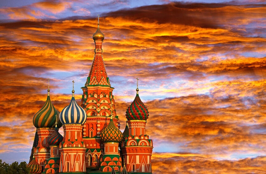 The colorful domes of St. Basil's Cathedral in Moscow, Russia, stand against a dramatic sky with vivid orange clouds at sunset, making it one of the most vibrant destinations for travelers around the world.