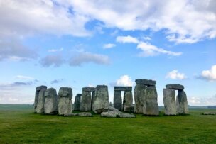 Stonehenge, a prehistoric monument of standing stones, stands majestically on Britain's Land, seen on a grassy field under a mostly cloudy sky.
