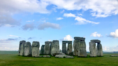 Stonehenge, a prehistoric monument of standing stones, stands majestically on Britain's Land, seen on a grassy field under a mostly cloudy sky.