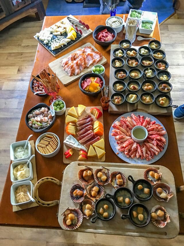 A table is filled with various food items, including seafood, cheeses, crackers, sliced meats, fruits, vegetables, and assorted dips—presented in bowls, trays, and plates—perfect fuel for planning your next epic hike through Patagonia.
