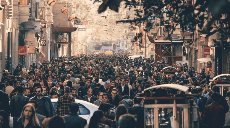 A crowded street filled with people walking in various directions, with shops and buildings lining both sides, feels like stepping into a favorite scene from an adventure short film.