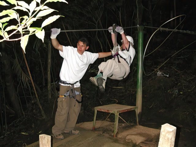 Two individuals are seen engaging in a wild zip-lining adventure at night. One person is gliding on the zip line, while the other is standing next to them, possibly offering assistance. This thrilling moment is a perfect highlight for any adventure BLOG about Wild Things.