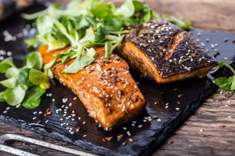 Two grilled salmon fillets topped with greens and sesame seeds rest on a dark slate platter, set on a rustic wooden table—a culinary delight that could easily be part of your travel adventures in Ireland.