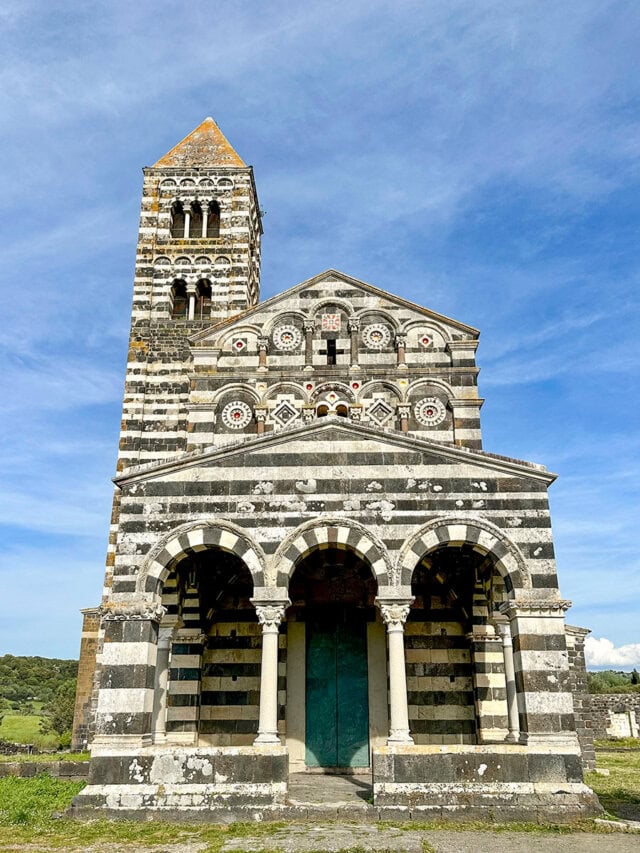 Set against a blue sky, this striped medieval church with its tall bell tower and intricate facade beckons travelers seeking island adventures in Corsica.