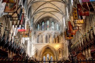 Explore the interior of a gothic cathedral in Dublin, showcasing high vaulted ceilings, stunning stained glass windows, and colorful flags adorning the upper walls—truly a must-see destination for travel enthusiasts seeking captivating things to do.