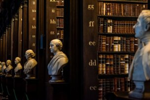 The library's interior, reminiscent of Dublin's rich history, features busts of historical figures on pedestals lining a wooden aisle. Shelves filled with old, leather-bound books and labeled sections in the background make it one of the city's must-see attractions.