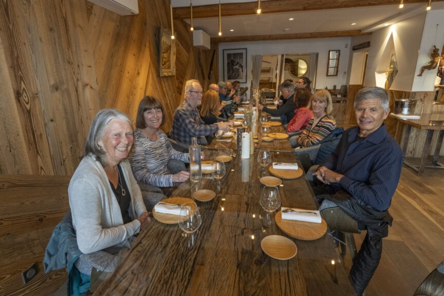 In a cozy restaurant, amidst the warm hues of autumn, a group of people sits around a long wooden table set with plates, glasses, and napkins. Their conversation drifts from hiking adventures to the breathtaking views from Mont Blanc.