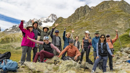 A group of people posing happily on a rocky terrain with mountains in the background, some sporting hiking gear and holding walking sticks, all enjoying the crisp Autumn air as they admire Mont Blanc's majestic beauty.
