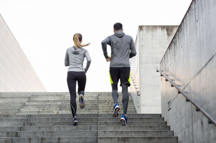 Two people in athletic clothing are training as they run up outdoor concrete stairs, heading away from the camera.
