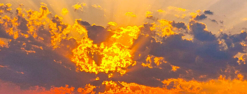 A fiery orange sunset with dark clouds scattered across the sky, illuminated by rays of sunlight, mirrors the majestic spectacle of the Great Elephant Migration.