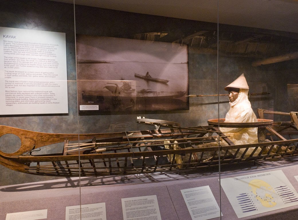 A museum display in Juneau features a traditional wooden kayak with an Inuit mannequin dressed in historic clothing, surrounded by informational plaques and historical images—a must-see for those seeking unique travel things to do.