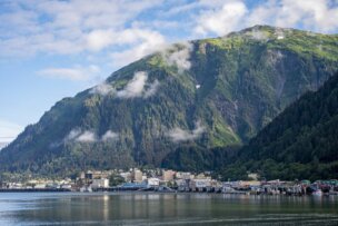 Nestled at the base of a large green mountain, Juneau offers stunning views where clouds and city reflect in calm waterfront waters—a must-see on any travel list for those seeking unique things to do.