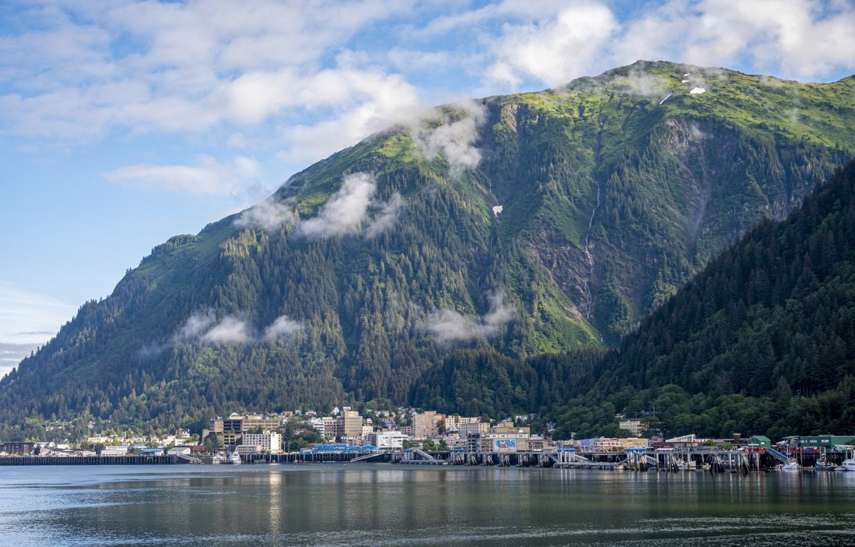 Nestled at the base of a large green mountain, Juneau offers stunning views where clouds and city reflect in calm waterfront waters—a must-see on any travel list for those seeking unique things to do.