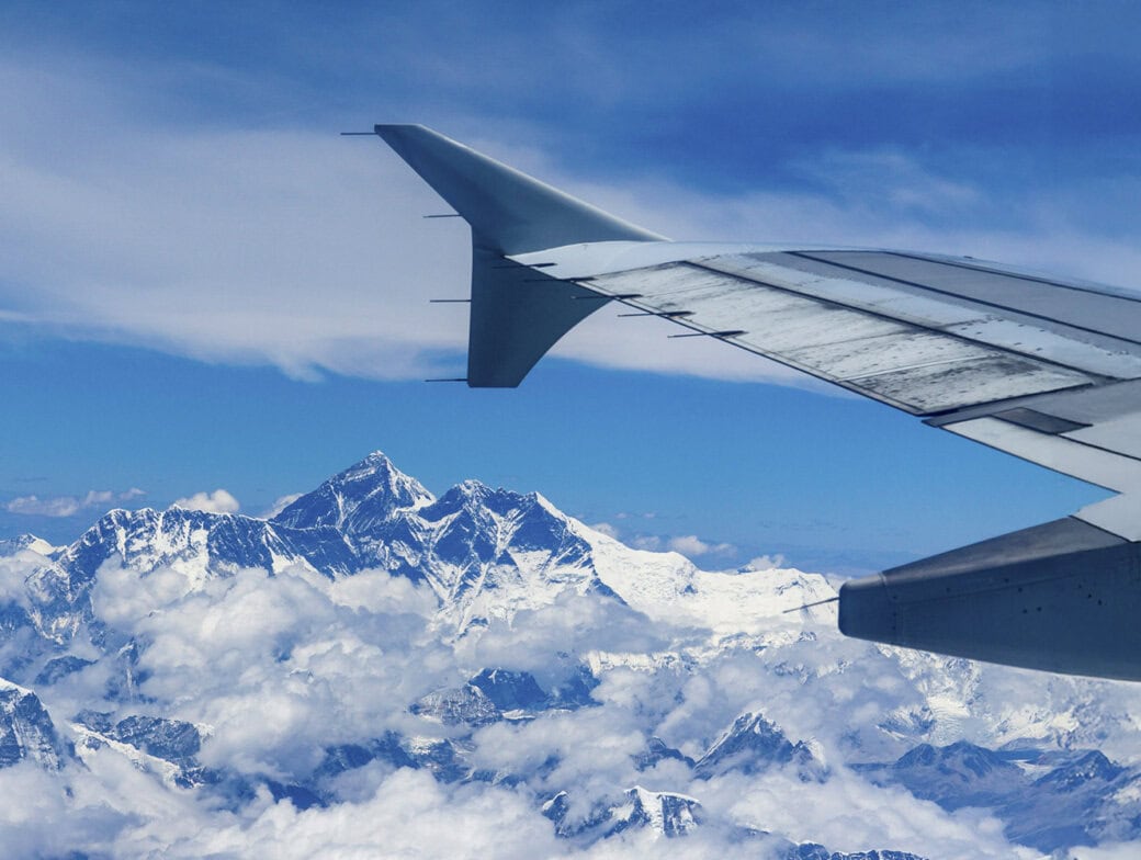 View from an airplane window showing the aircraft wing and snow-covered mountains, including Mount Everest, under a blue sky with scattered clouds—a breathtaking start to discovering things to do in Kathmandu.