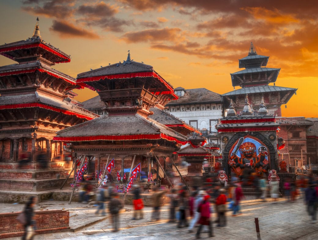 People walk past historic temples and a large deity statue in Durbar Square, Kathmandu, Nepal, during sunset—a must-see among the many things to do in Kathmandu.