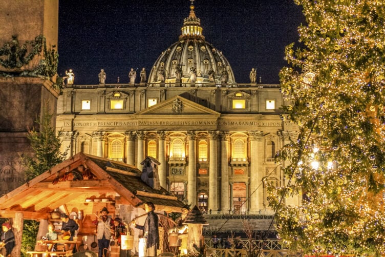 A nativity scene and Christmas tree are illuminated in front of St. Peter's Basilica at night in Vatican City, making the holiday season the best time to visit Italy for a magical experience.
