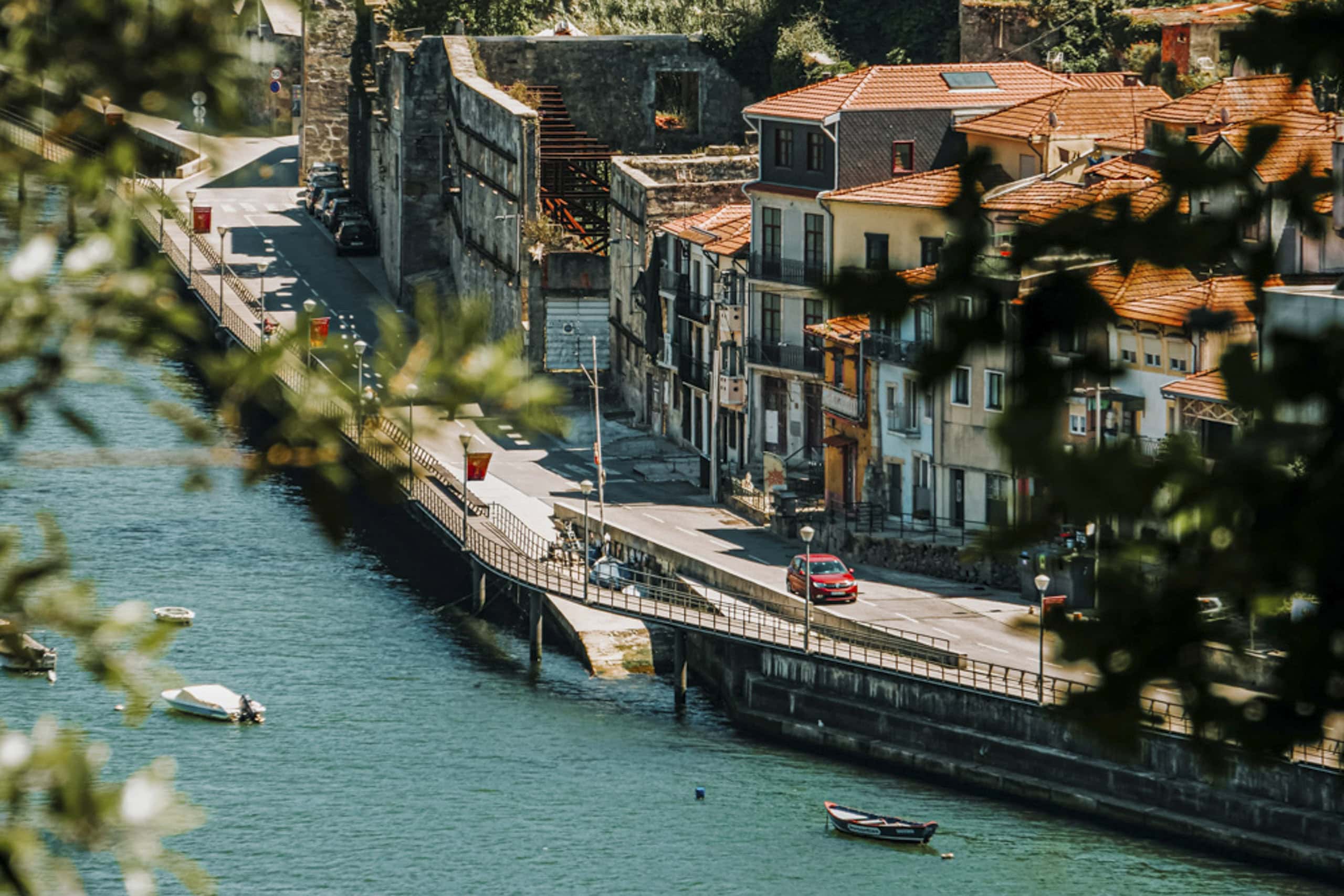 A riverside street in Real Portugal lined with red-tiled roof buildings, a few cars along the road, and small boats floating on the water—perfect for exploring with an expert guide after a day of hiking Portugal’s scenic trails.