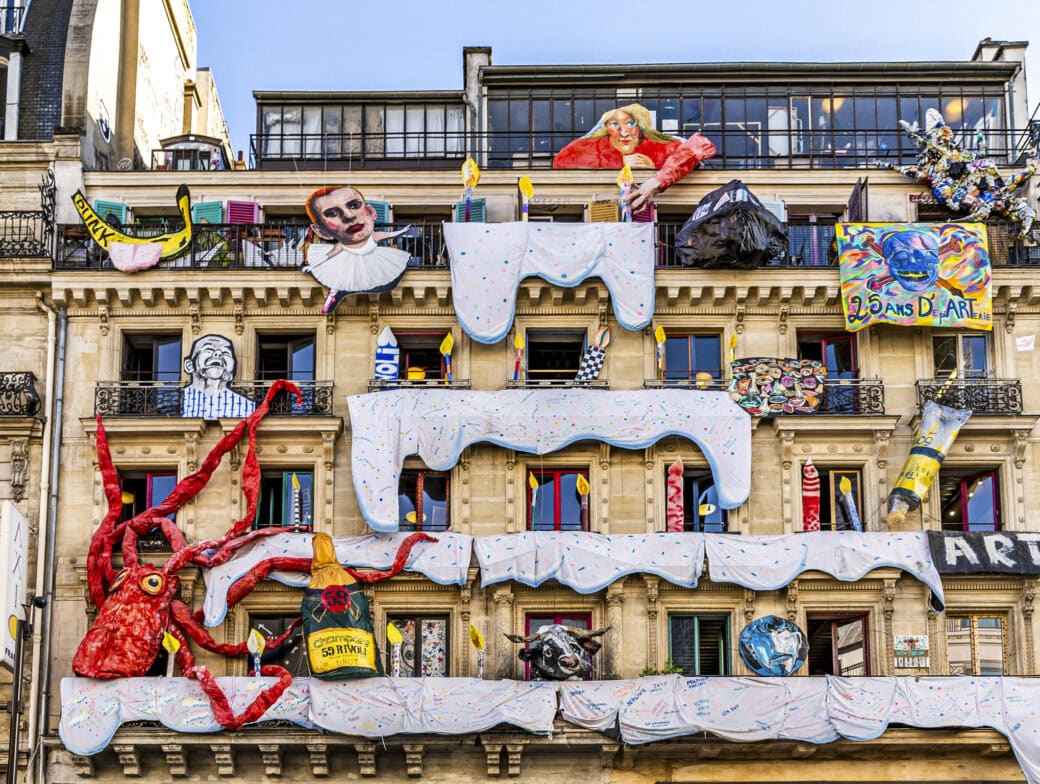 A Paris building façade, decorated with large colorful sculptures—like an octopus, faces, and draped white fabric resembling icing or snow—is one of the quirky Paris attractions perfect for your list of things to do in Paris.