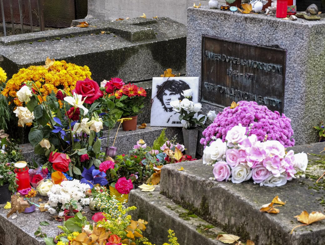 A gravestone surrounded by colorful flowers, candles, and a black-and-white portrait of a person, with fallen leaves scattered on the ground—one of the unique things to do in Paris for those interested in its atmospheric cemeteries.
