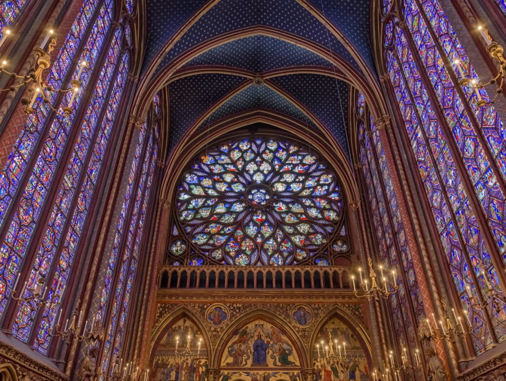 Interior view of a Gothic cathedral, featuring tall stained glass windows, a large rose window, pointed arches, and ornate chandeliers—one of the must-see Paris attractions for anyone interested in Gothic architecture and Paris travel.