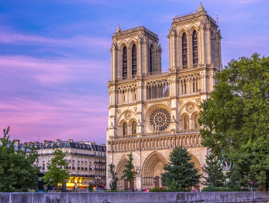 Notre-Dame Cathedral in Paris stands with its twin towers and rose window, framed by trees under a pink and purple evening sky—a true highlight among Paris Attractions for your Paris Travel list.