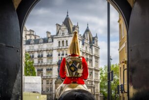 A Horse Guards soldier in ceremonial uniform sits on horseback, facing ornate historic buildings in London England, viewed through an arched gateway—a timeless scene among top things to do in London.