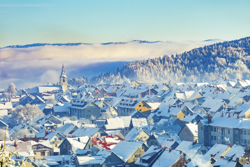 A town in Croatia with snow-covered rooftops, a church with a tall steeple, and distant forested hills under a clear blue sky—it's the perfect scene to experience during the best time to visit.