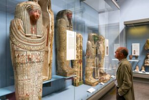 A man views ancient Egyptian sarcophagi and artifacts displayed in a museum glass case—one of the fascinating things to do in London for history enthusiasts.