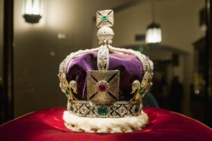 A jeweled crown with a purple velvet cap and fur trim displayed on a red cushion under bright lighting—a must-see for London tourism and anyone seeking iconic things to do in London.