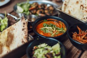 A table set with various Indian dishes, including naan bread, curry in a black bowl, salad, and vegetable sides—perfect for experiencing one of the top Things to Do in London England.