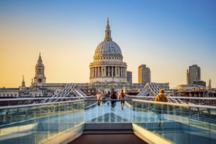People walking on the Millennium Bridge toward St. Paul’s Cathedral at sunset, with modern buildings in the background—a classic scene among the top things to do in London, England.
