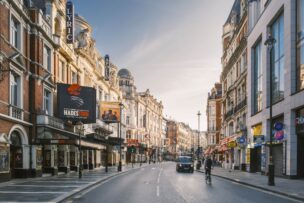 A street in London’s West End featuring theaters, shops, a black cab, and cyclists beneath clear skies—one of the classic London attractions with vibrant show signs and endless things to do in London England.