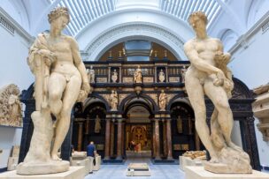 Two large marble statues of male figures stand in a spacious museum gallery with arched ceilings and classical architectural details—an inspiring sight among the many things to do in London.