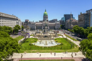 A wide view of the Argentine National Congress building in Buenos Aires with its green dome, surrounded by Plaza del Congreso, fountains, trees, and city buildings—one of the top things to do in Argentina on a clear blue sky day.