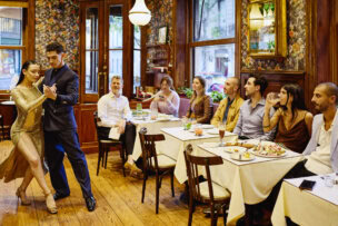 A couple performs a dance in front of seated diners inside a Buenos Aires restaurant with wooden floors and floral-patterned walls—a classic Argentina experience and one of the top things to do in the city.