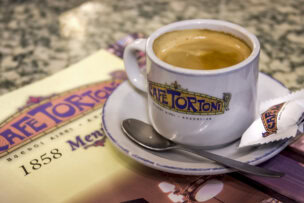 A cup of coffee on a saucer with a spoon, next to a sugar packet and a Café Tortoni menu on a marble table—a classic Buenos Aires experience and one of the must-try things to do in Argentina.